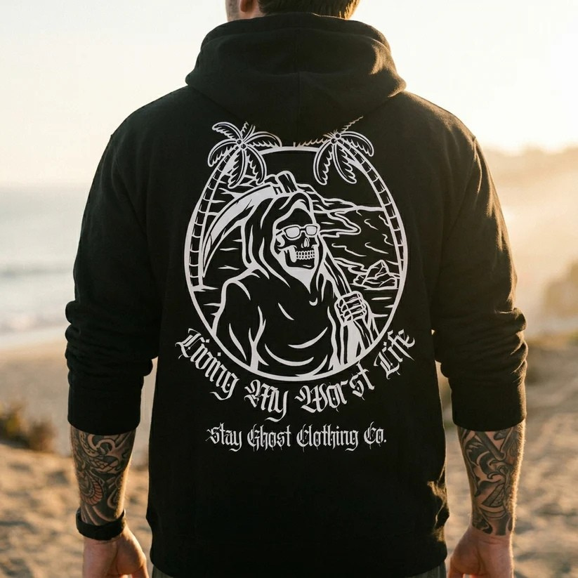 Person wearing a black hoodie with a graphic design on the back at the beach.