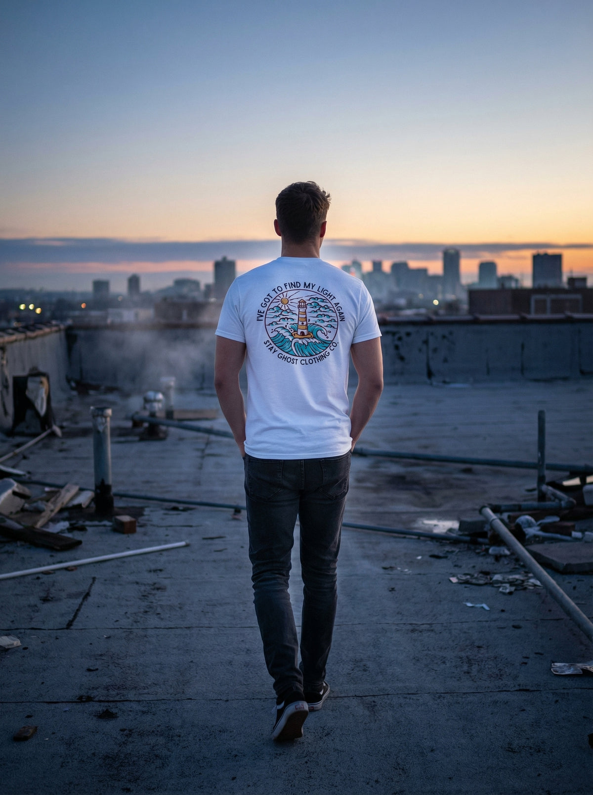 Person standing on a rooftop with a cityscape view at sunset, wearing a white t-shirt with graphics.